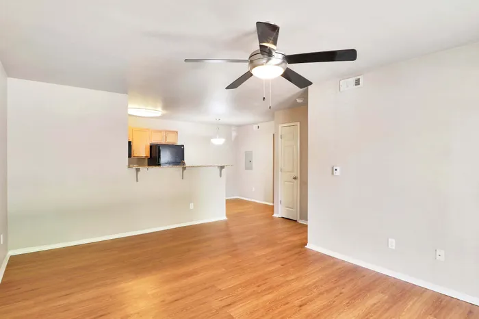 Inviting open-concept living area featuring elegant wood flooring, a sleek ceiling fan, and a modern kitchen with light cabinetry.