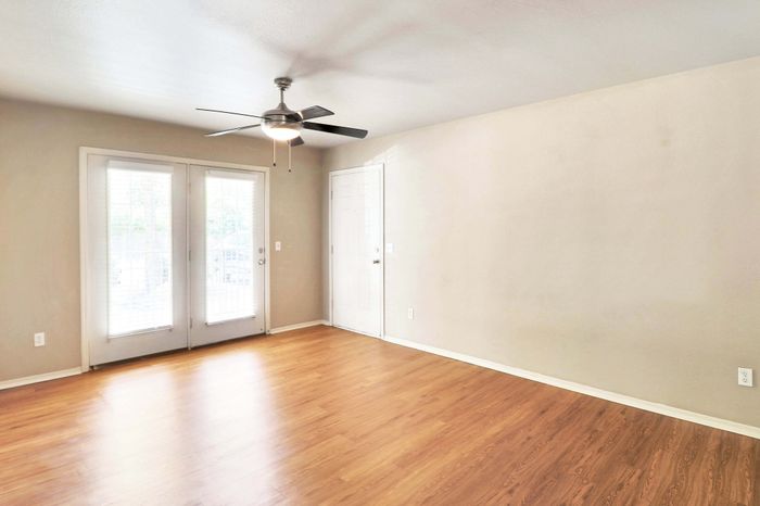 Bright and spacious living room with elegant wood flooring, large windows, and a modern ceiling fan.