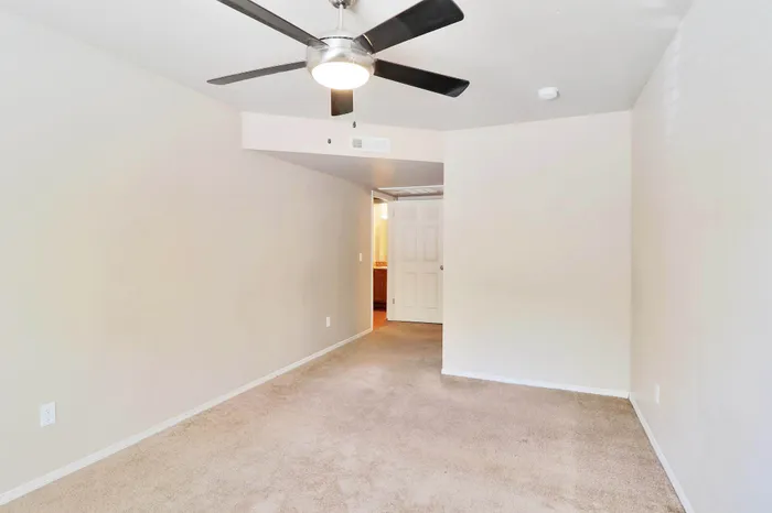 Bright and spacious room with soft carpet flooring and modern ceiling fan, offering a welcoming and cozy atmosphere.