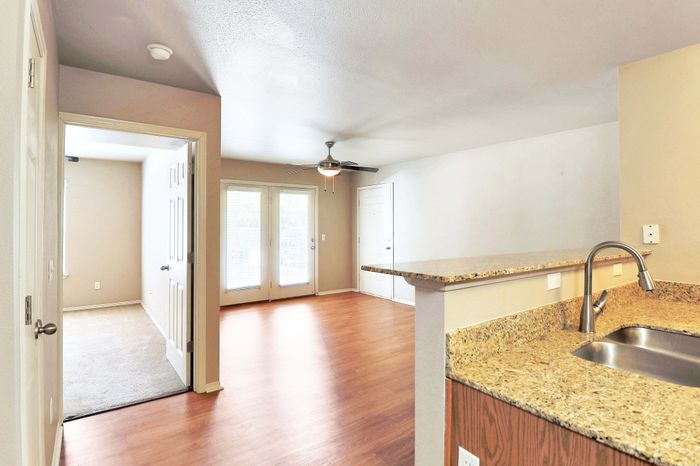 Bright open-concept living space featuring a modern kitchen with granite countertops, hardwood floors, and ample natural light from large windows.