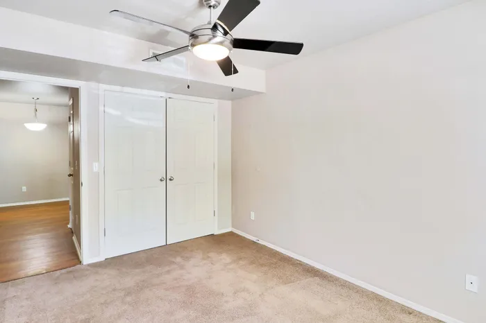 Bright, cozy room featuring soft carpet flooring, a sleek ceiling fan, and an elegant double door closet. Ideal for modern living.