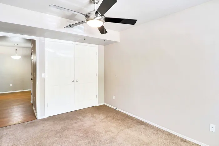 Bright, inviting bedroom with modern ceiling fan, plush carpet, and ample closet space.