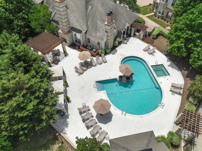 Luxurious outdoor pool area with stylish lounge chairs, umbrellas, and a hot tub, surrounded by lush greenery and elegant architecture.