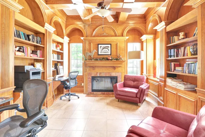 Elegant home office with rich wood paneling, built-in bookshelves, cozy fireplace, and natural light streaming through large windows.