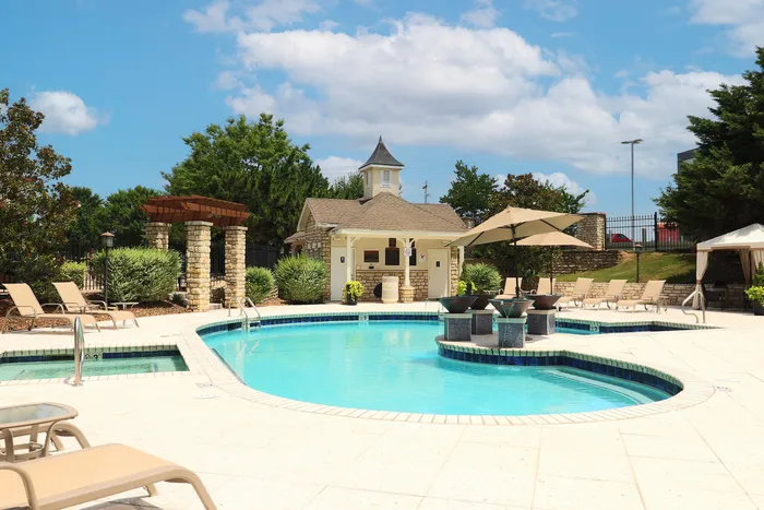 Inviting outdoor pool area featuring stylish lounge chairs, shaded pergolas, and a quaint pool house, surrounded by lush greenery under a vibrant blue sky.