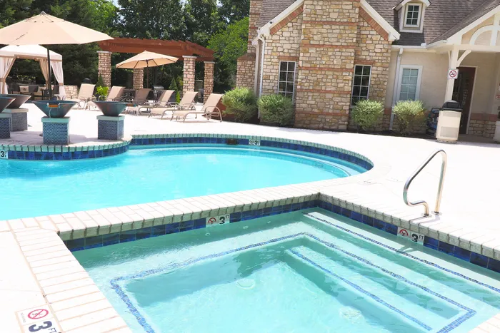 Inviting outdoor pool area with elegant lounge chairs, umbrella-covered seating, and a charming stone building backdrop, perfect for relaxation and leisure.