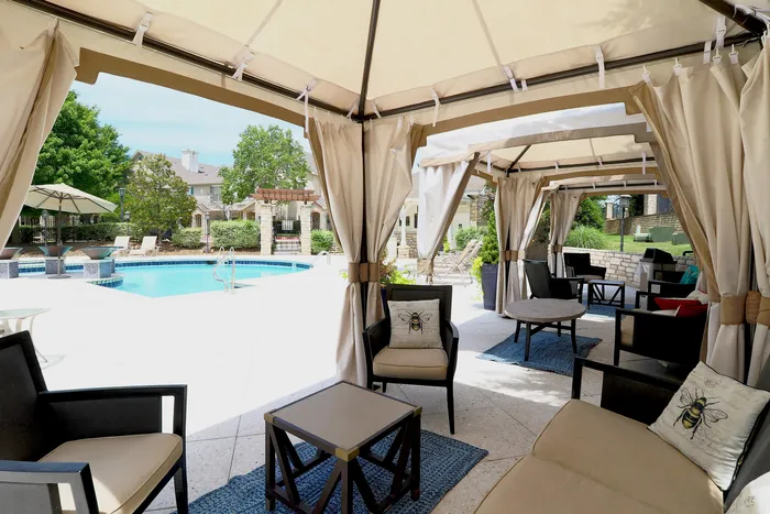 Luxurious outdoor lounge with elegant cabanas overlooking a sparkling blue pool, surrounded by lush greenery.