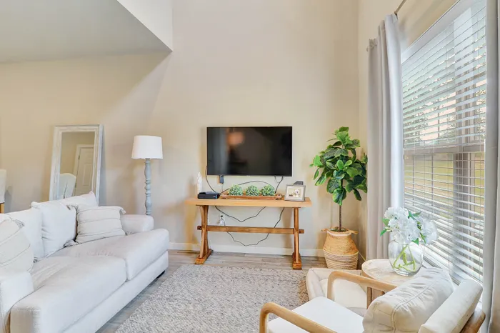 Inviting living room with cozy cream sofa, large window bringing in natural light, and a stylish wooden TV stand accented by modern decor.