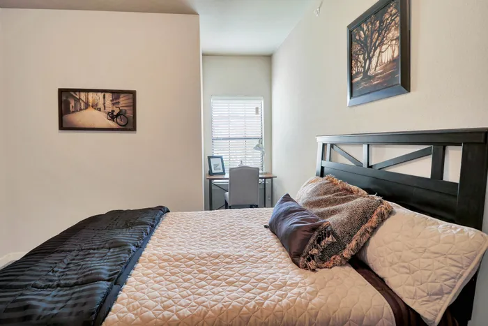 Cozy and stylish bedroom with modern decor, featuring a plush bed, elegant artwork, and a compact workspace by the window for natural light.