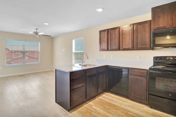 Bright, open-concept kitchen and living area with modern lighting, sleek dark wood cabinetry, and elegant countertops inviting natural light through large windows.