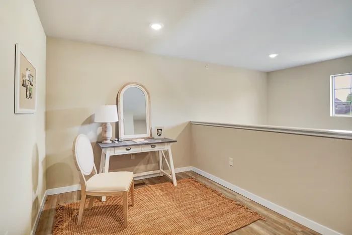Charming nook with a stylish desk, elegant mirror, and cozy chair on a warm woven rug.
