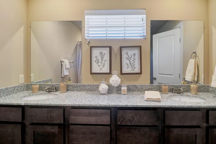 Elegant bathroom featuring dual sinks, granite countertops, and stylish framed art accents.
