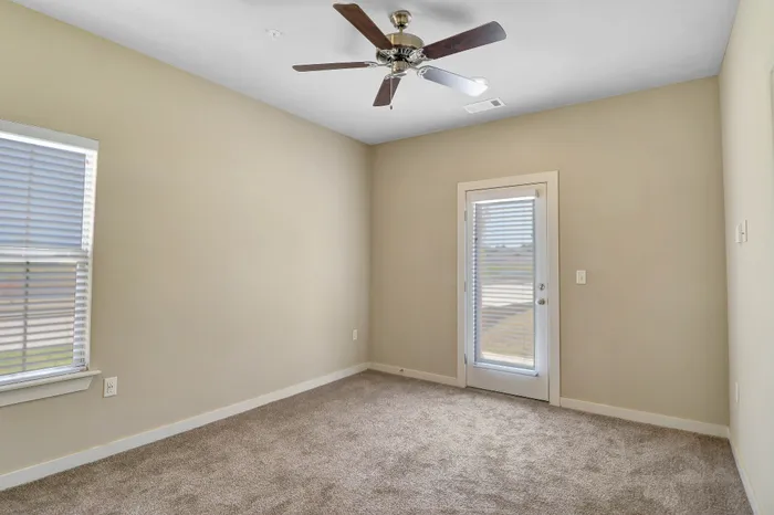 Bright and inviting room with soft carpeting, modern ceiling fan, and French door leading to outdoor space, perfect for relaxation.