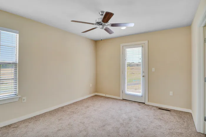 Bright and inviting room with a ceiling fan and plush carpet, featuring two large windows and a door leading to a scenic view, perfect for a cozy retreat.