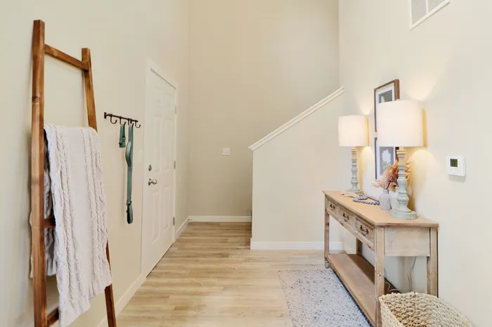 Inviting entryway with warm wood floors, elegant console table with lamps, and decorative accents, enhanced by a cozy woven basket and a chic wooden ladder with a white throw.