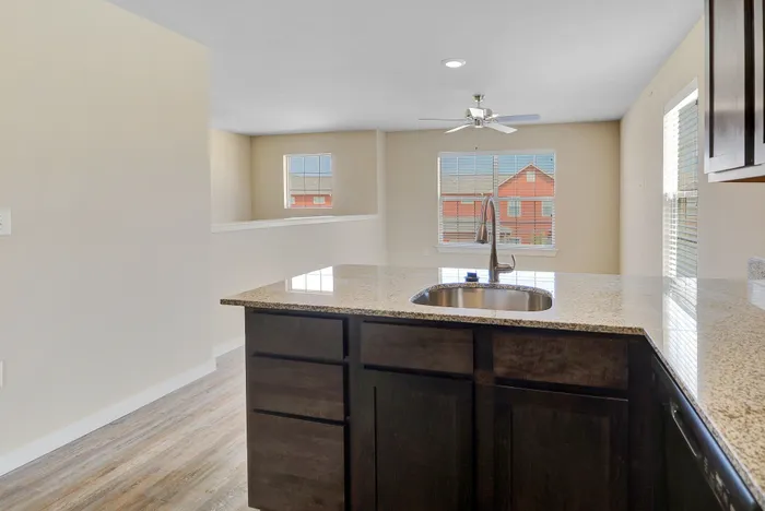 Bright open kitchen with granite countertops and a modern faucet, seamlessly connecting to a sunlit living area with large windows.