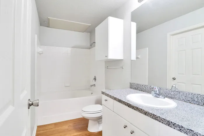 Bright, modern bathroom featuring sleek cabinetry, elegant granite countertop, and a pristine white tub with shower.