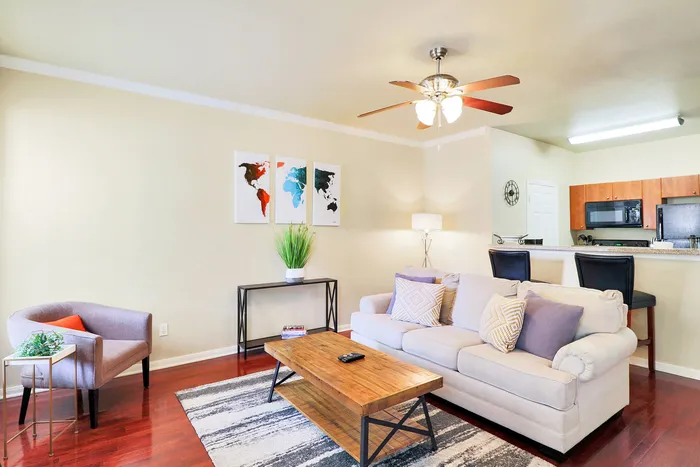 Bright and inviting living room with elegant decor, featuring a cozy sofa, stylish coffee table, wall art, and an open kitchen with modern appliances.