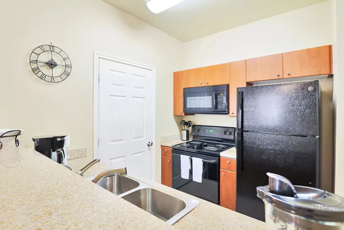 Modern kitchen featuring sleek black appliances, wooden cabinets, and a double sink, under warm lighting with stylish wall clock.