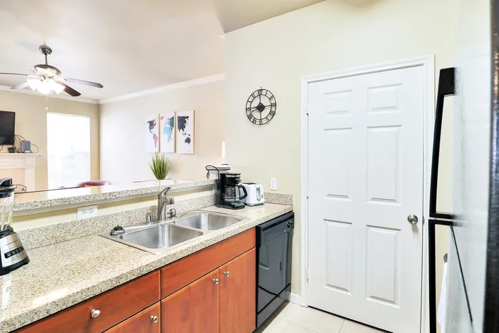 Modern kitchen with elegant granite countertops, stainless steel sink, and sleek appliances leading into a bright living room with contemporary decor.