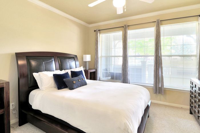 Bright and airy bedroom with a large bed, stylish dark wooden headboard, and elegant decor, featuring floor-to-ceiling windows for natural light.
