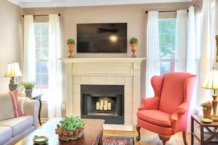 Cozy living room with elegant fireplace, stylish red armchair, large windows, and soft ambient lighting.