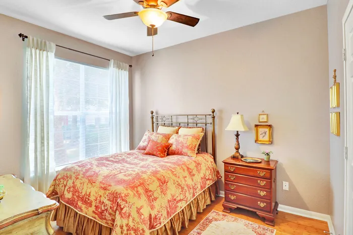 Inviting and cozy bedroom with elegant ceiling fan, soft natural light streaming through large window, and warm-toned bedding complementing classic wooden furniture.