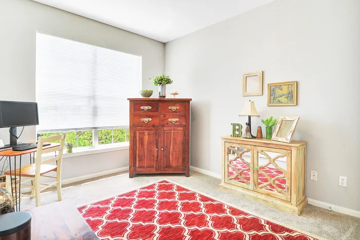 Bright and inviting home office with large window, elegant red-patterned rug, and stylish wooden furniture for a perfect work-from-home setting.