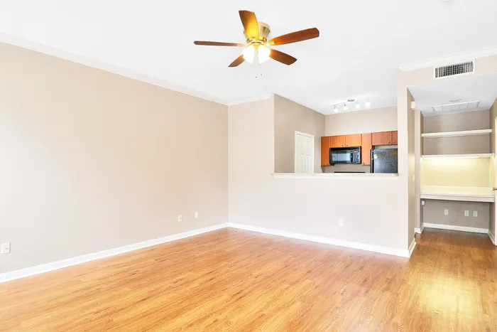 Bright and inviting living area with wood flooring, modern kitchen, and a charming ceiling fan.