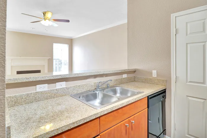 Modern kitchen with granite countertops, double sink, and open view to a cozy living room with a ceiling fan and bright natural light.