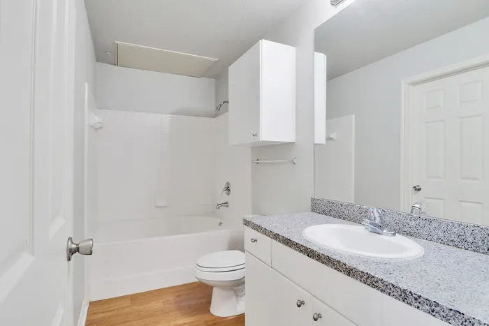 Bright and modern bathroom with sleek granite countertop, white cabinetry, and a clean bathtub featuring elegant fixtures.