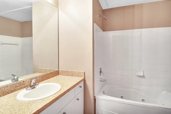 Elegant bathroom featuring a sleek granite countertop with a modern sink and a relaxing bathtub surrounded by pristine white tiles.