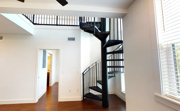 Elegant apartment with a sleek spiral staircase, hardwood floors, and abundant natural light through large windows.