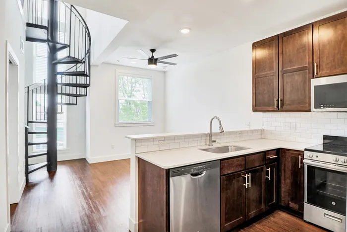 Modern apartment interior with sleek kitchen, stainless steel appliances, and elegant spiral staircase. Bright and spacious for luxurious living.