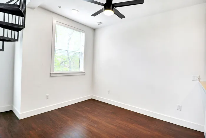 Bright and airy room featuring sleek dark wood floors, a modern ceiling fan, and a spiral staircase, perfect for a contemporary lifestyle.