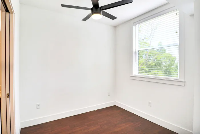 Bright and modern bedroom with sleek ceiling fan, large window, and rich hardwood floors.