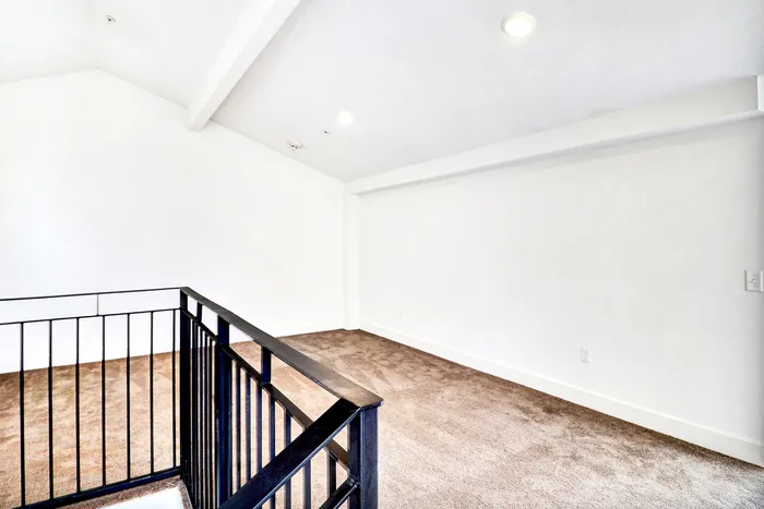 Modern loft area with plush carpeting and a sleek black railing, providing a bright and spacious feel.