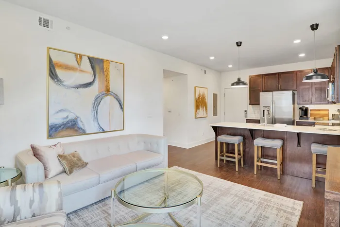 Modern open-concept living area with elegant artwork, cozy seating, and stylish kitchen island in a bright, contemporary apartment.