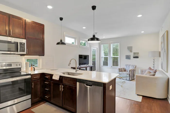 Modern open-concept kitchen and living area with sleek stainless steel appliances, elegant lighting, and cozy seating next to large windows.