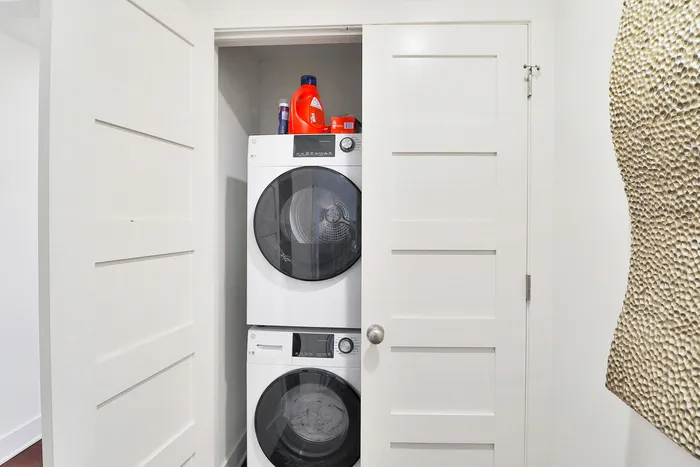 Modern laundry nook with stacked washer and dryer, hidden behind sleek white doors, offering space-saving convenience.