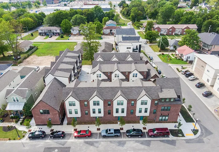 Charming aerial view of a modern townhouse complex with stylish red brick and white facades, nestled in a lush suburban setting.
