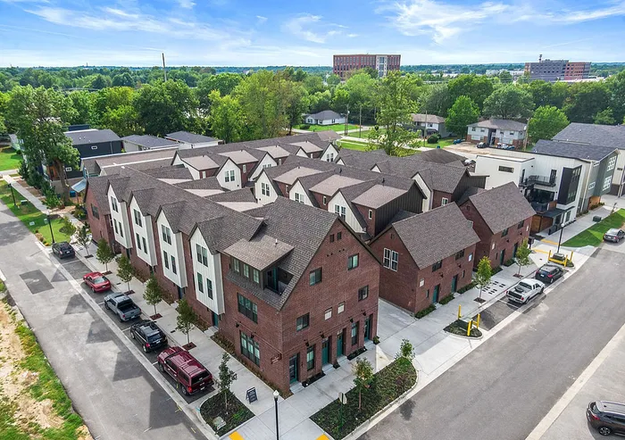 Aerial view of a modern townhouse community with charming brick exteriors, surrounded by lush greenery and well-maintained streets.