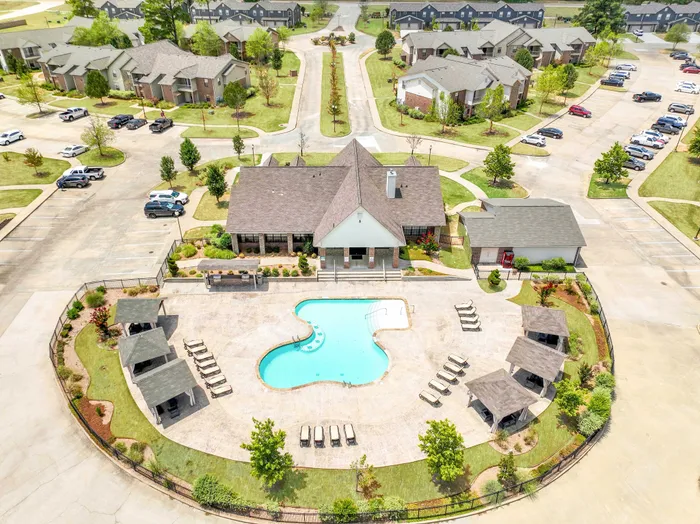 Aerial view of a vibrant apartment complex showcasing a modern clubhouse, inviting swimming pool, and spacious surroundings with ample parking and lush green landscaping.