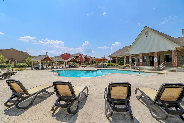 Inviting outdoor pool area with stylish lounge chairs and charming covered seating, set against a backdrop of vibrant buildings and a clear blue sky.