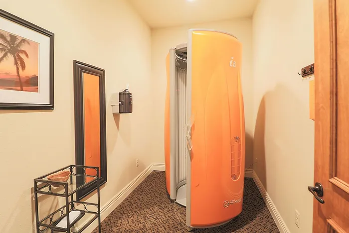 Modern tanning room featuring an orange stand-up tanning booth, elegant wall art, and sleek decor accents.
