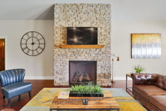 Inviting living room with a stone fireplace, sleek TV, and stylish decor including a modern clock and abstract art.