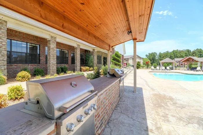 Inviting outdoor pool area with modern grills under a stylish wooden canopy, surrounded by lush greenery and elegant architecture.
