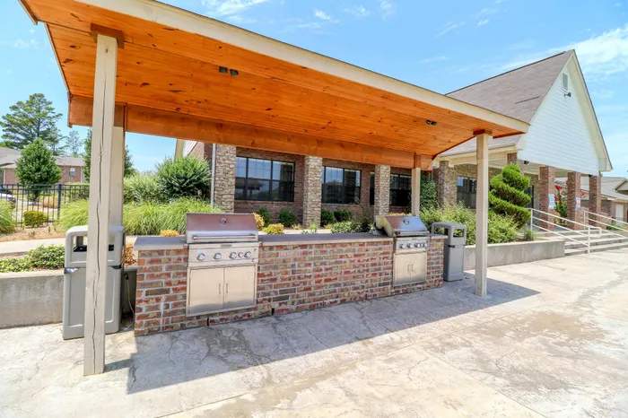 Inviting outdoor BBQ area with modern grills under a stylish wooden canopy, perfect for entertaining in a lush, landscaped setting.