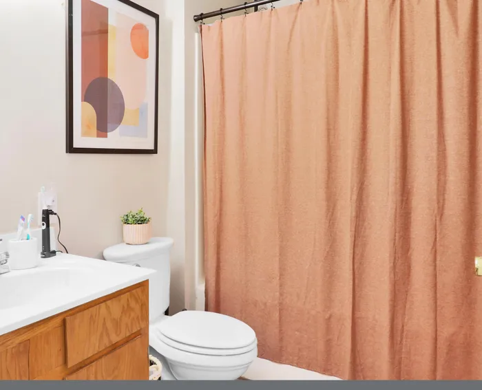 Charming bathroom with modern fixtures, warm peach shower curtain, artistic wall decor, and sleek wooden vanity.