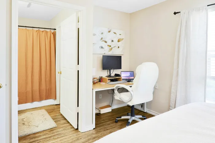 Bright and cozy home office space with elegant decor, featuring a comfortable white chair and a neatly organized desk seamlessly connected to the main bedroom.